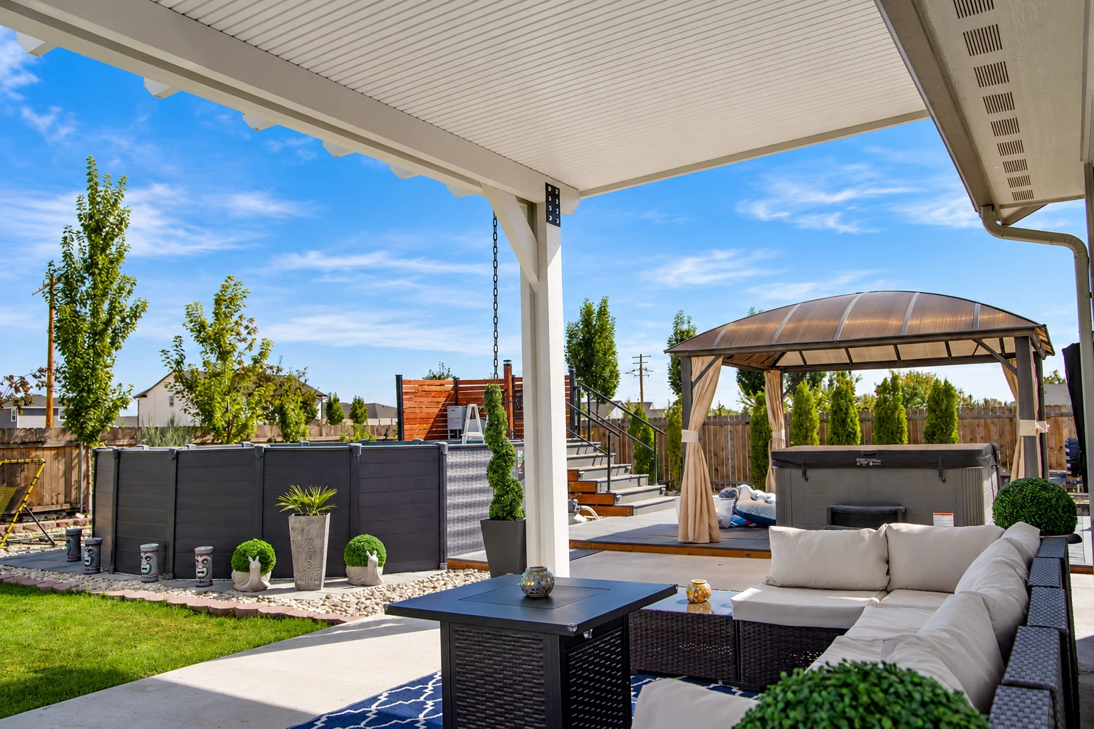 Covered patio with a white paneled roof, outdoor sectional seating and a hot tub in the yard.