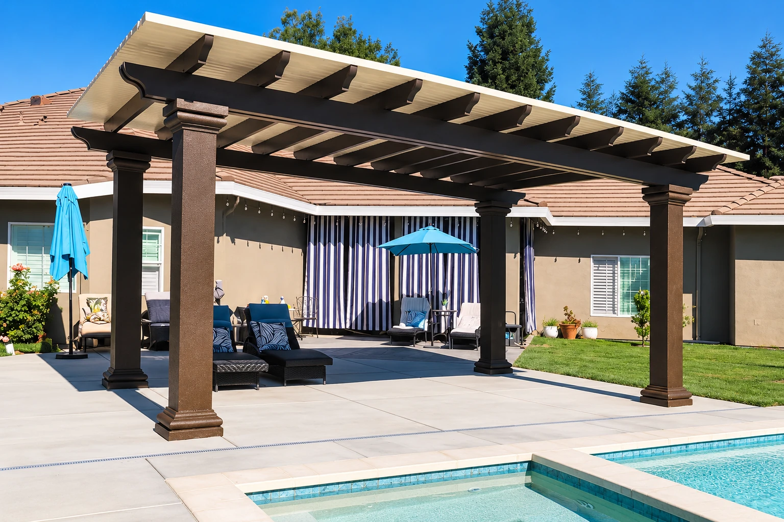 A covered patio with a white paneled roof on dark columns, furnished seating, and a swimming pool in the foreground.
