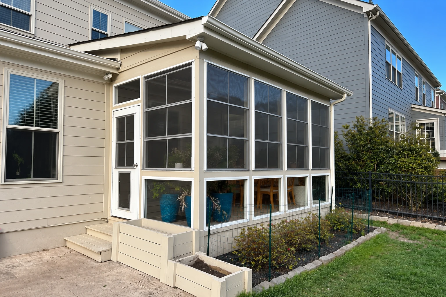 Enclosed patio with dark screened panels, white trim, a side entry door, and raised garden beds.