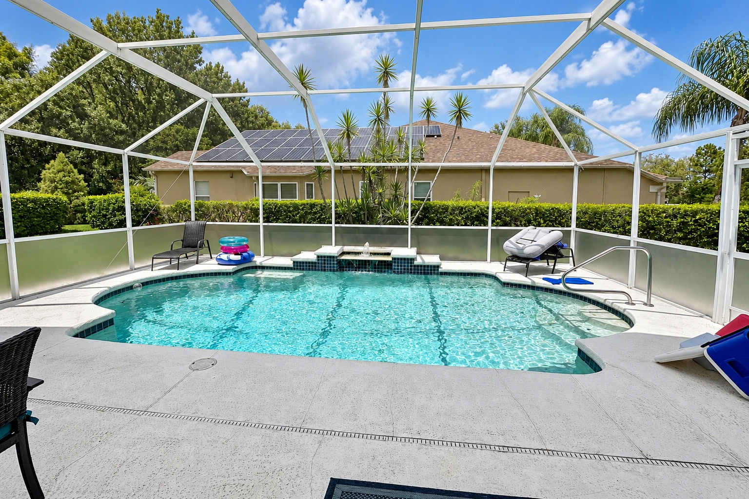 Screened pool enclosure with a white metal frame, turquoise water, and lounge chairs under a sunny sky.