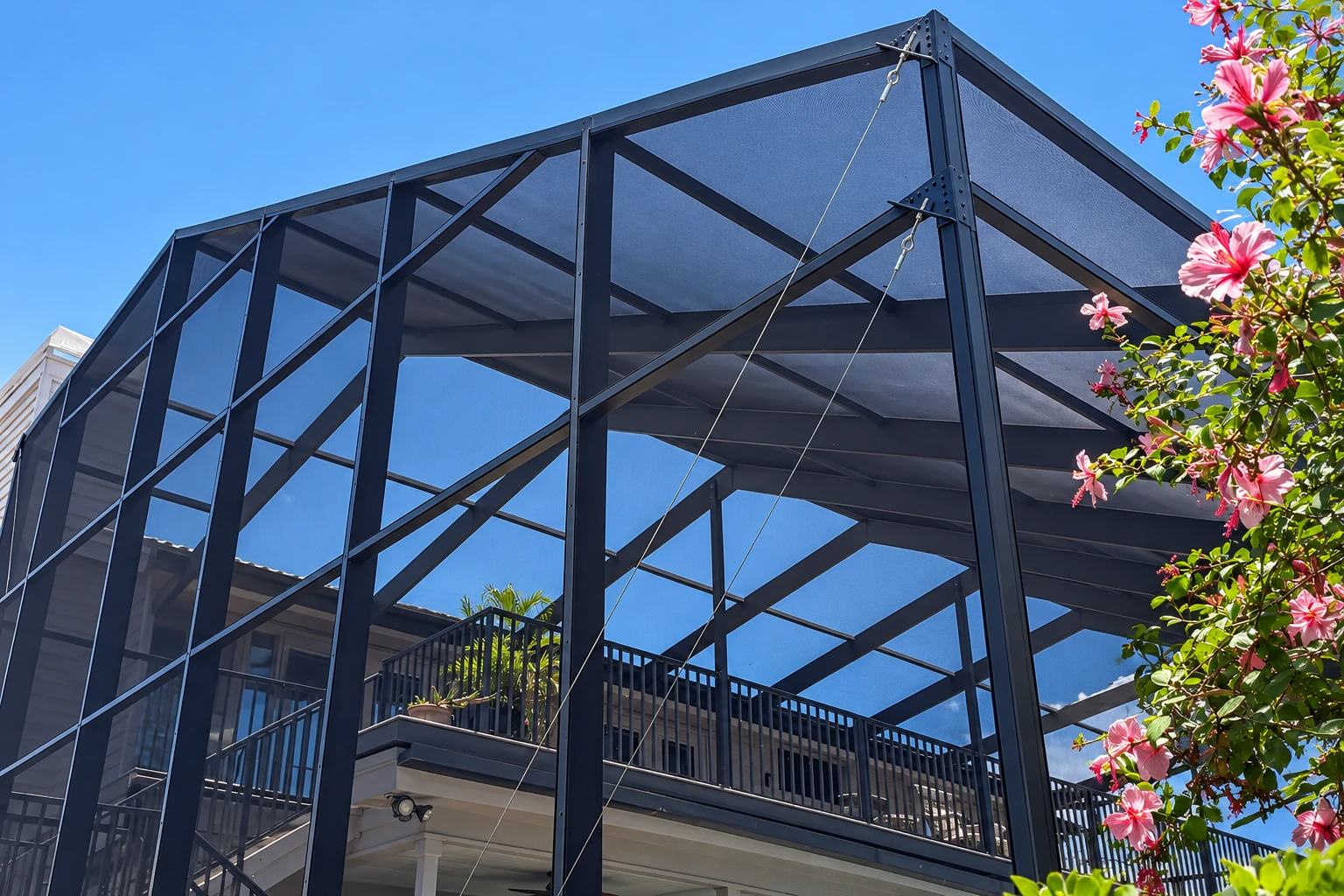 Screen room with dark metal framing and mesh panels, viewed from below against a blue sky.