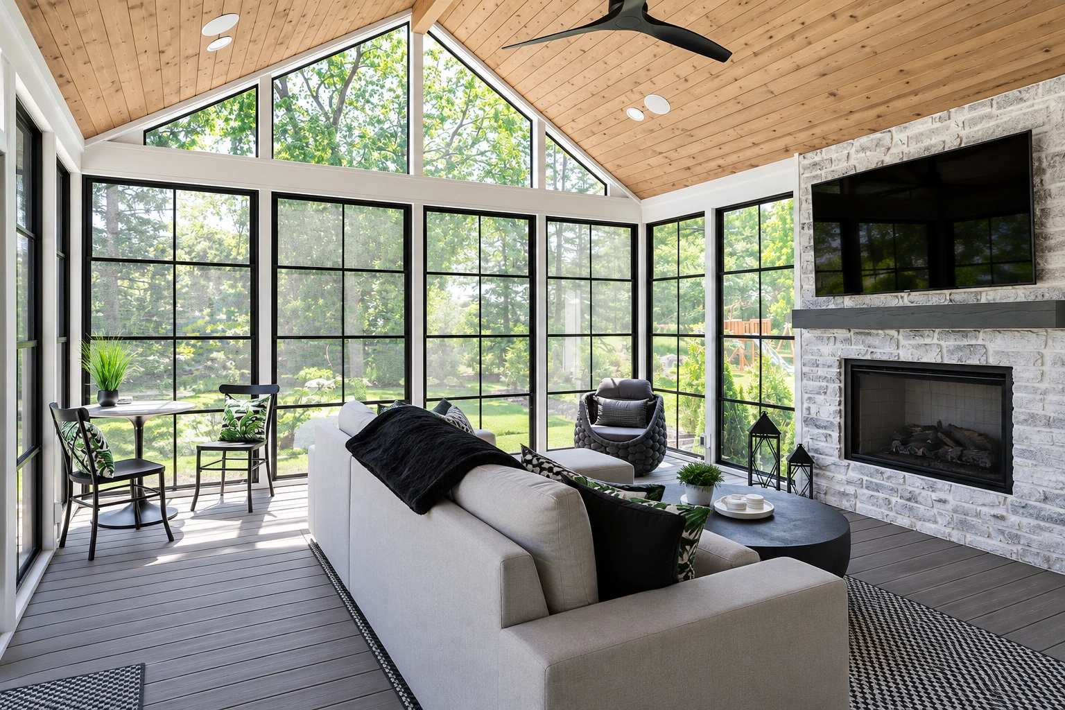 Three-season sunroom with a vaulted wood ceiling, black-framed windows, a stone fireplace, and modern seating.