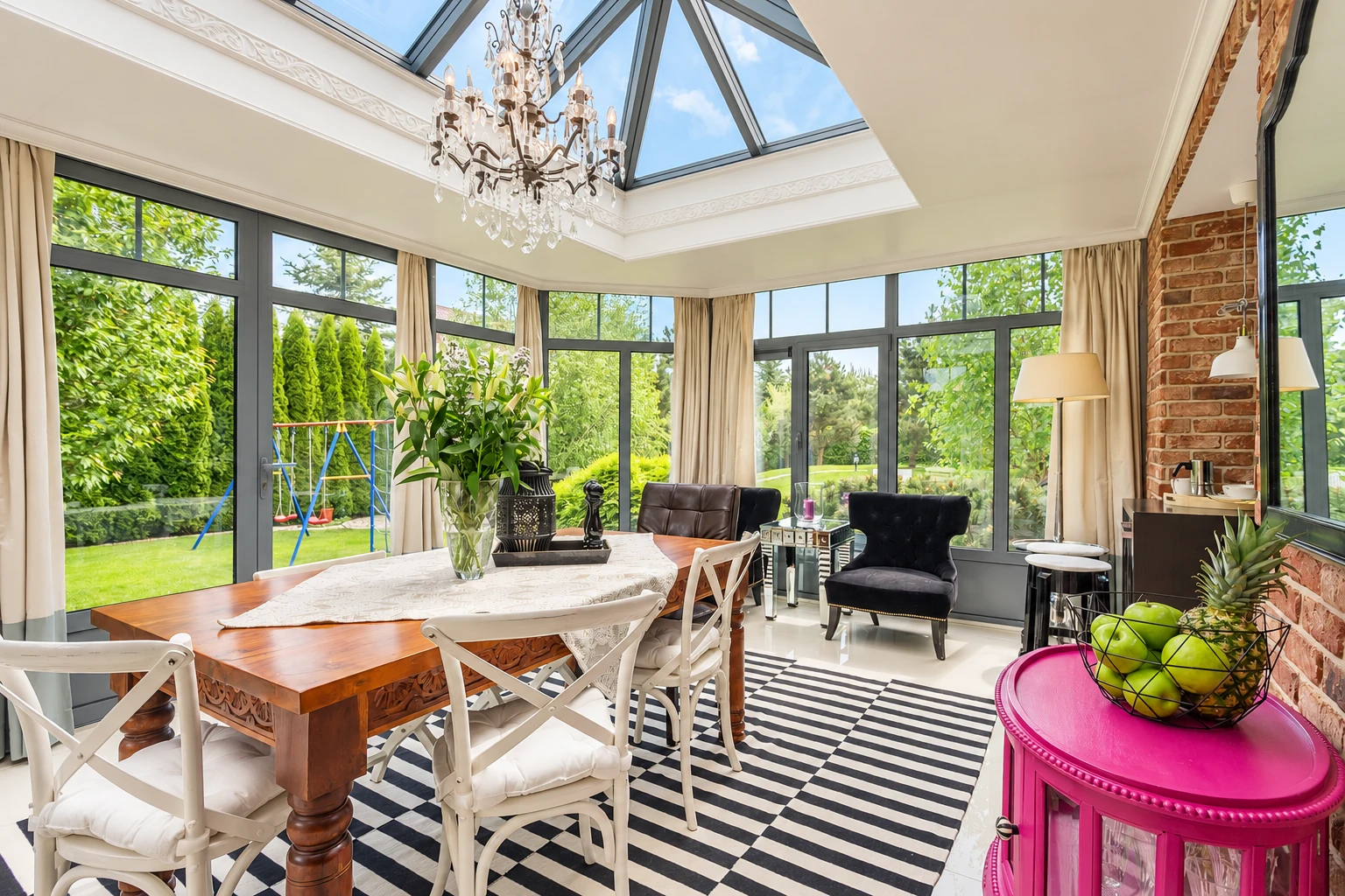 Sunroom with a glass-paneled roof, dark-framed windows, dining table, and brick accent wall.